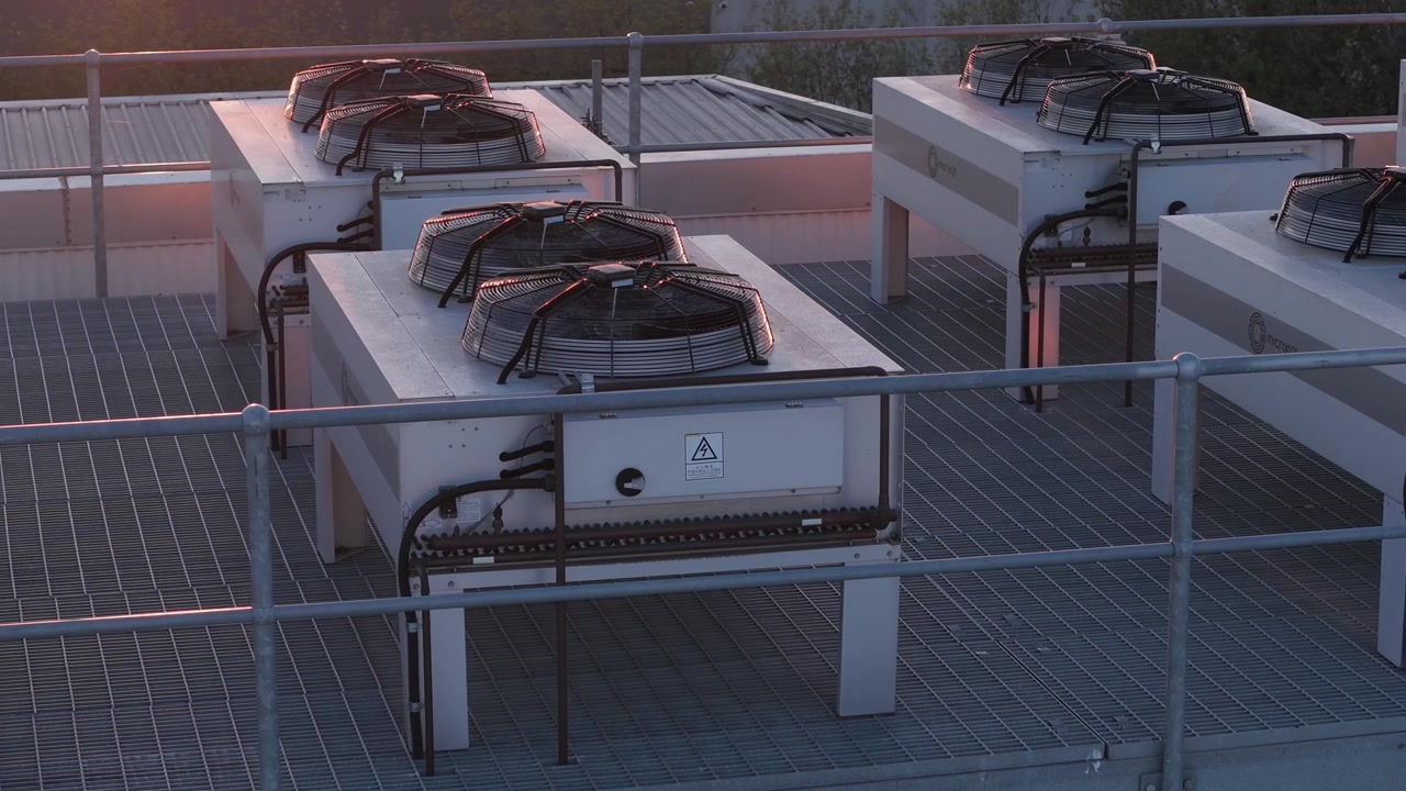 Industrial air conditioning units with spinning fans on a rooftop during sunset