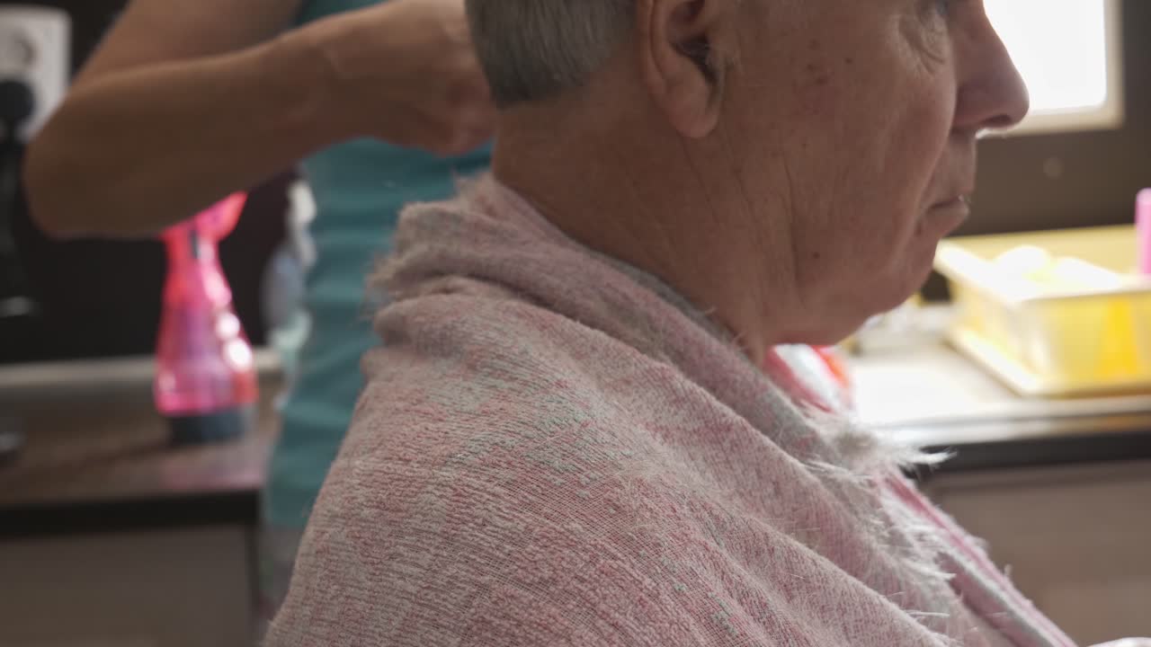 Close up head profile of house bound senior grey haired man having haircut in home kitchen. Copy space.