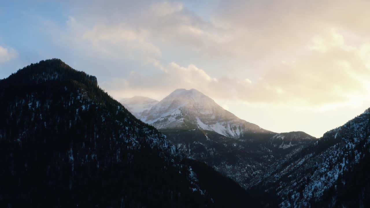time-lapse de drones aéreos de un paisaje invernal del monte timpanogos en el fondo rodeado por un bosque de pinos durante la puesta de sol desde el embalse de bifurcación de tibble congelado en el cañón de bifurcación americana, utah