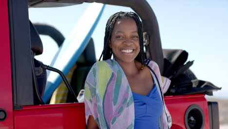 young african american woman smiles beside a red vehicle on a road trip