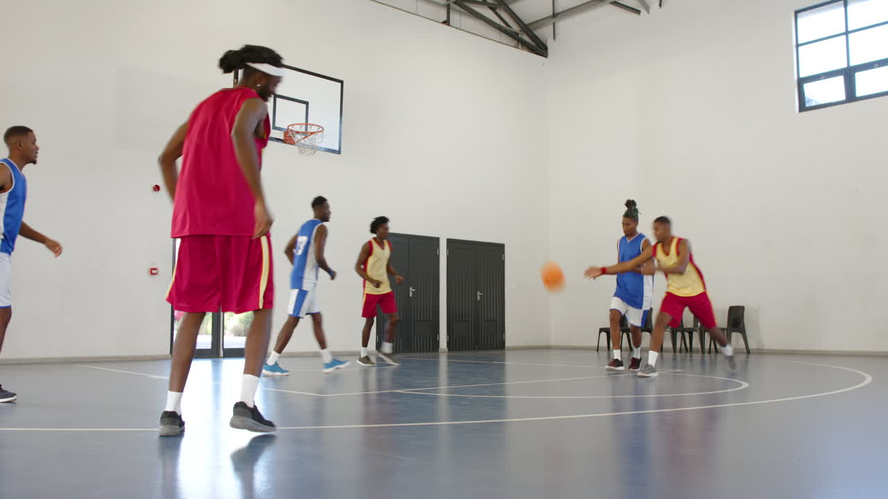 Giocatori di basket maschi multietnici che giocano a basket, passando e lanciando il pallone in palestra.