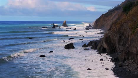 golven crashing surf zwart zand ruige kustlijn zonnige ochtend blauwe hemel mist laag gebruikelijke strand camping verloren kust pad california aerial drone pnw rotsblokken berghelling vooruit pan up