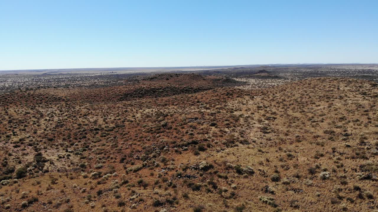 un plano general extremo que captura el paisaje de terreno arbustivo contra un cielo azul claro