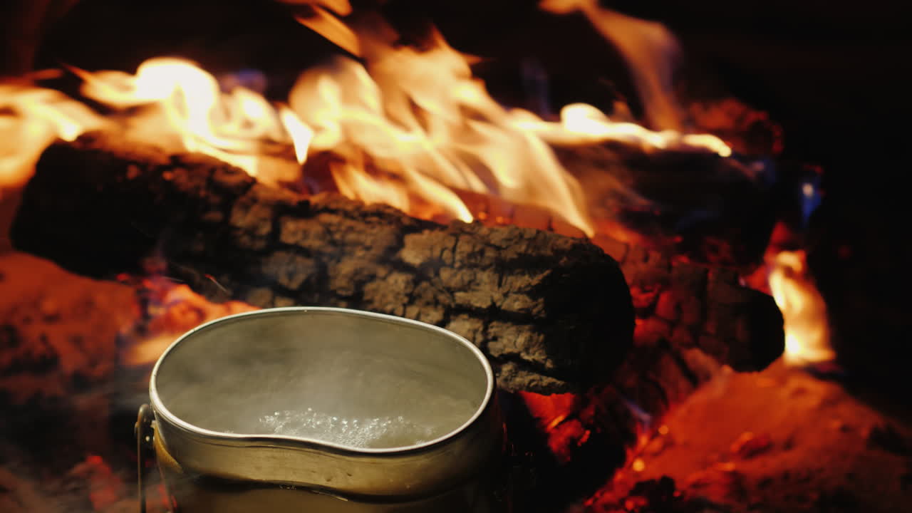 하이킹 4k 비디오에서 뜨거운 차와 음식을 준비하는 불 주위에서 캠프 주전자가 끓고 있습니다.