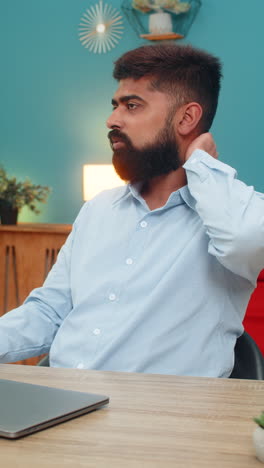 indian man closes laptop rubs stiff neck after long work hours feeling tired strained muscles indoor