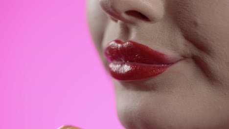 mujer lamiendo helado con su lengua, boca en primer plano en fondo rosa