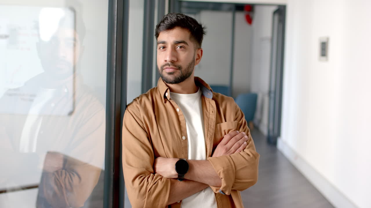 Confident man standing with arms crossed in modern office hallway