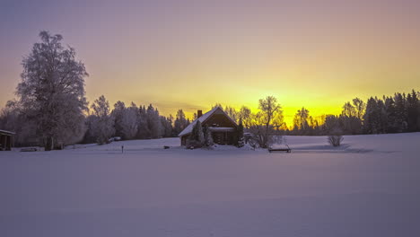 Golden-sunset-behind-cozy-wooden-cabin,-snowy-winter-wonderland