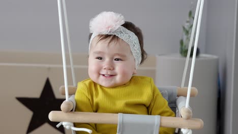 Cute-one-year-baby-sitting-in-door-frame-swing-and-changing-face-expressions-from-neutral-to-overexcited-and-joyful,-clapping-hands-and-move-from-side-to-side-smiling