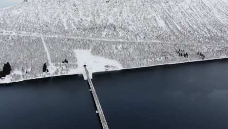 drone view in tromso area in winter flying over a fjord surrounded by white mountains and a bridge crossing in norway