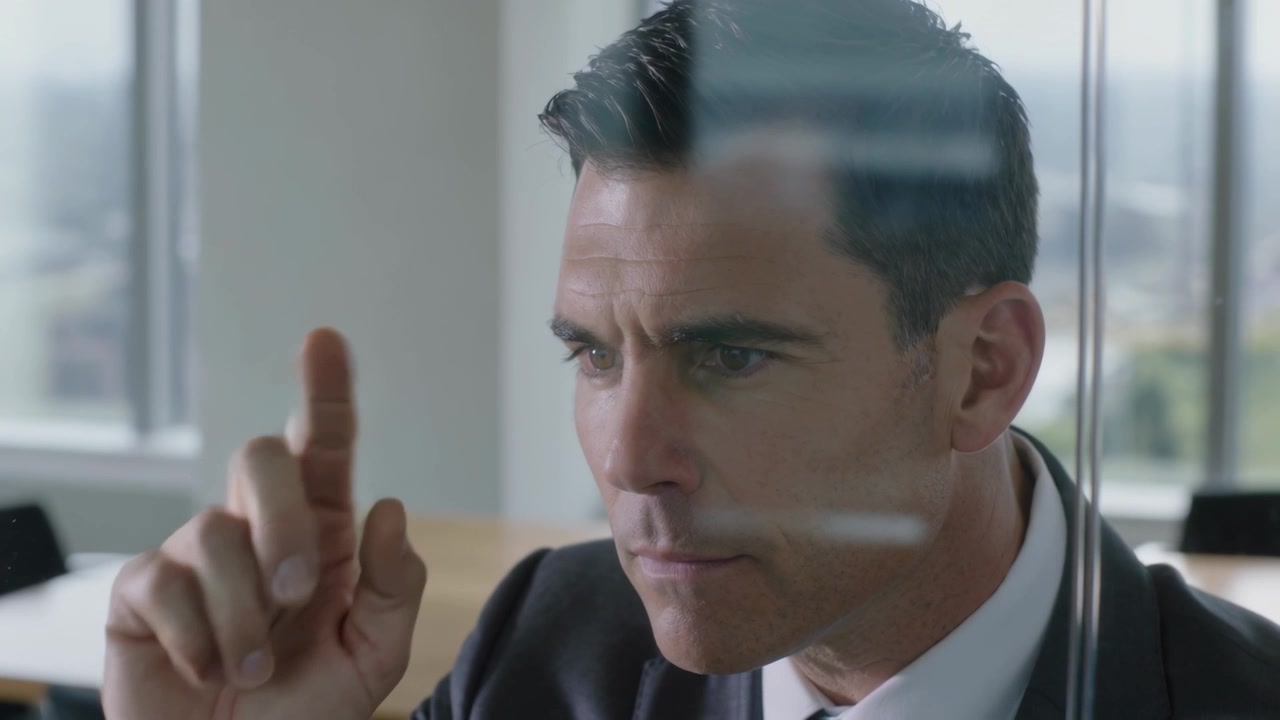 Raising right index finger, man in suit tracing glass lines in conference room, analyzing plan