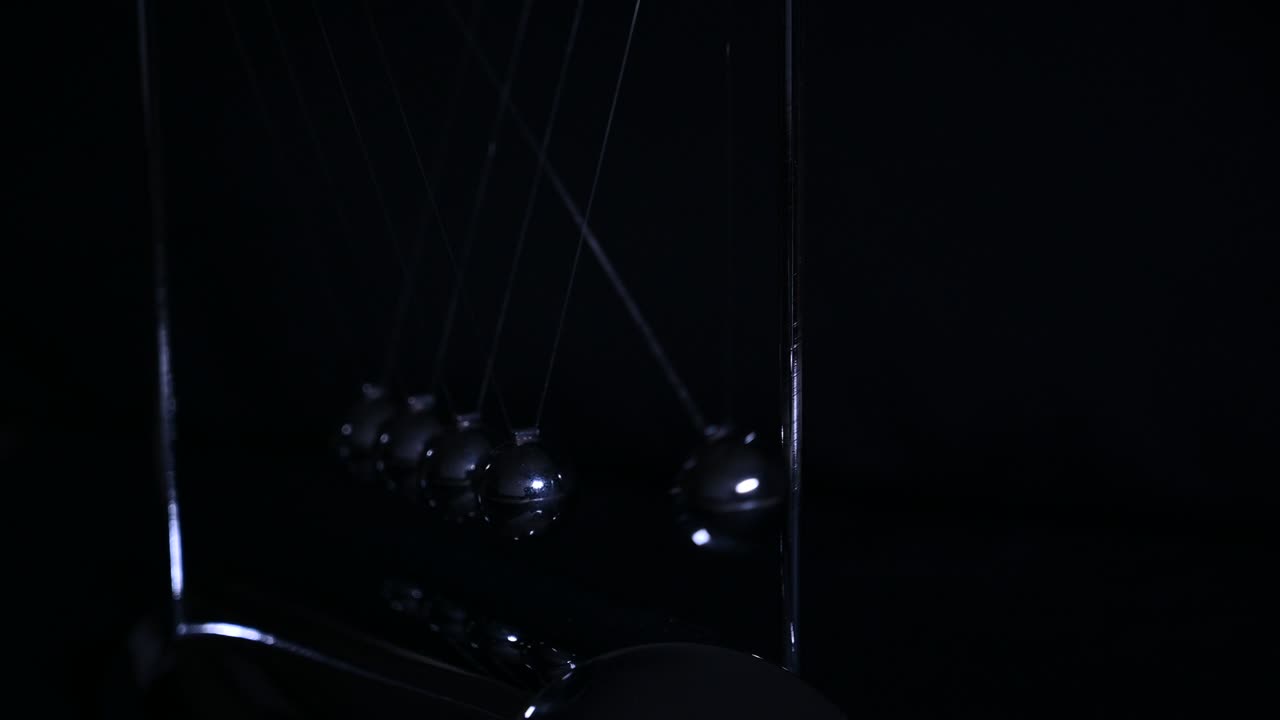 рука кладет ньютонскую колыбель, балансируя шары в темном тоне. физика движения и общие физические законы концепция действия и реакции, причина и следствие. шары ньютон.