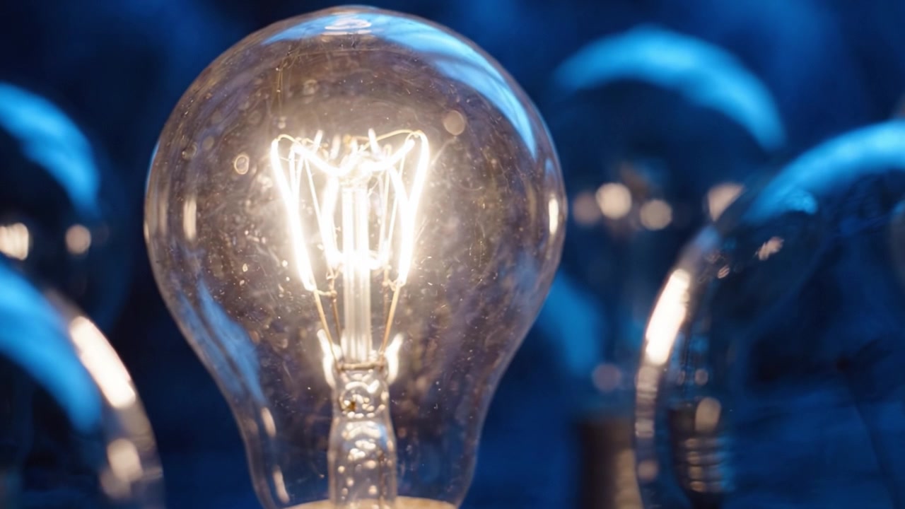 Lampadina illuminata in un ambiente scuro, che mostra il design in vetro e un bagliore caldo tra altre lampadine, riflettendo un tema di luminosità, tecnologia e innovazione
