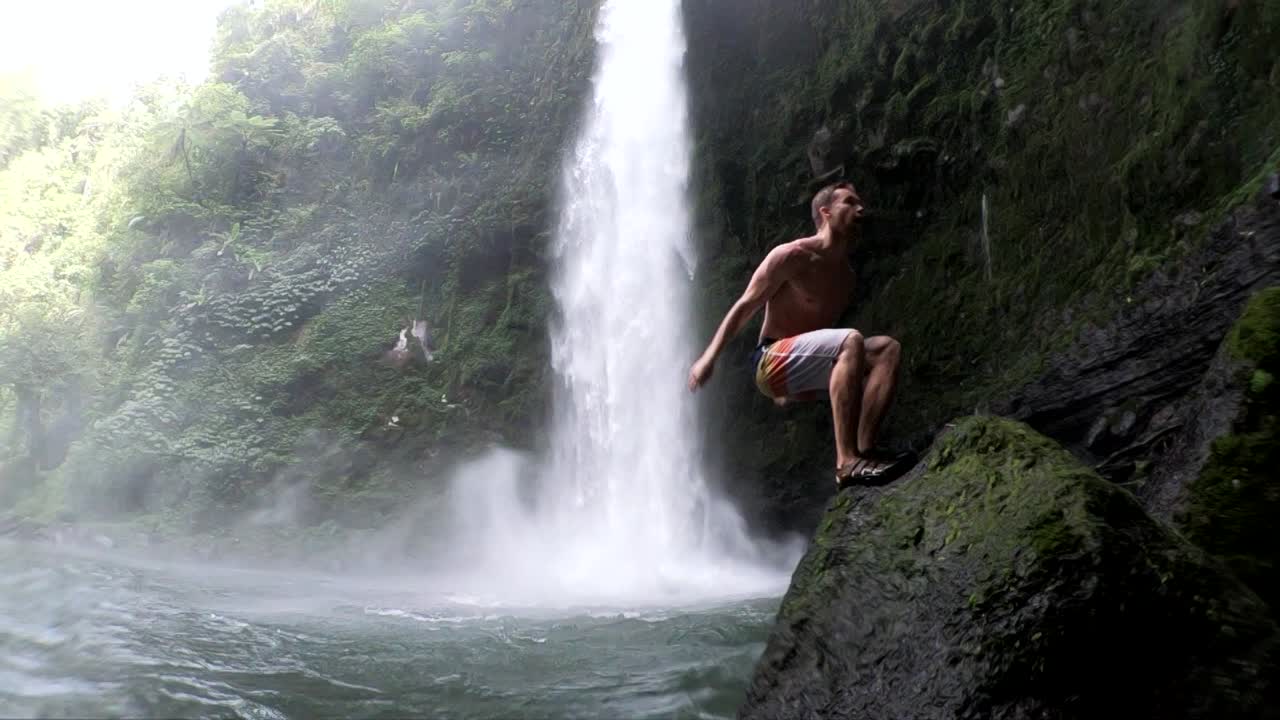 인도네시아 발리의 눙눙 폭포에서 물 속으로 공중제비를 하는 남자의 슬로우 모션 샷