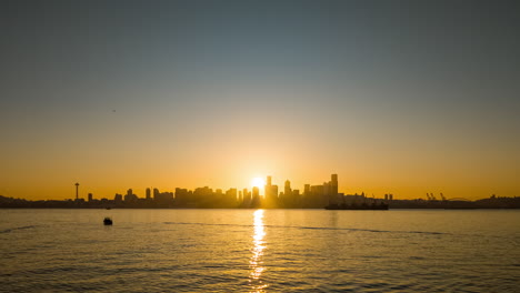 golden sunrise behind seattle skyline with soft reflections on the calm waterfront and silhouettes of buildings and boats. 4k time-lapse