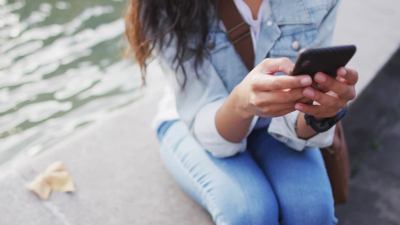 Woman tapping smartphone on ledge by water, generating animated world map showing technology data