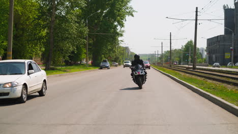 Biker-rides-fast-motorcycle-along-road-past-tram-route