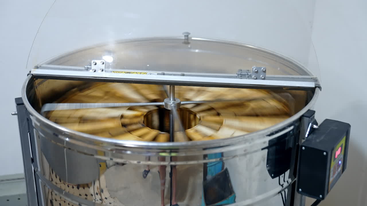 Metal centrifugal machine pumping organic honey. Honey extractor is spinning with frames to press out honey from honeycombs.