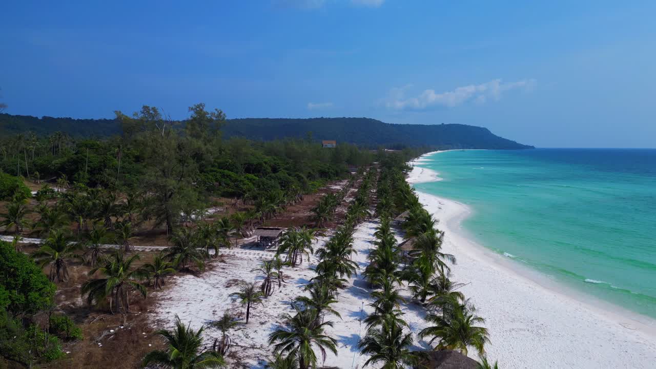 Sok San Beach with turquoise water washing the white sand, surrounded by palm trees and tropical vegetation. Unique aerial view flight dolly left drone
