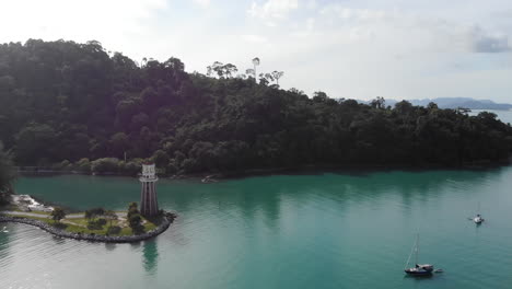 aerial pan reveal view of a lighthouse by a bay with turquoise water and boats