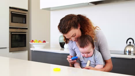 happy mother sitting with baby boy on lap playing with wooden toy