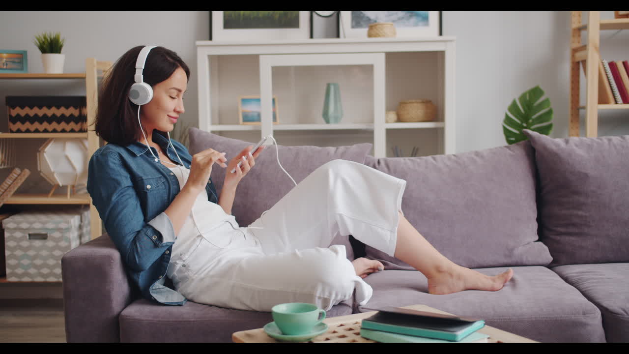 Woman relaxing on couch listening to music and using phone