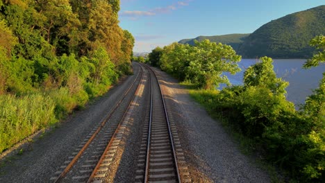 Aerial-drone-footage-of-the-metro-north-Hudson-Line-train-tracks-during-summer-next-to-the-Hudson-river-between-beacon-and-cold-spring,-new-york,-usa