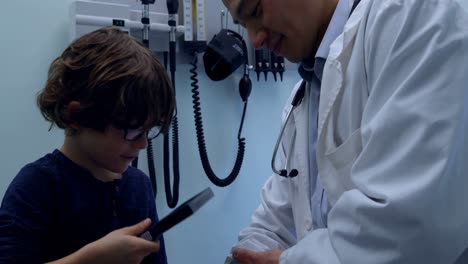 Vista-Lateral-De-Un-Paciente-Niño-Caucásico-Examinando-A-Un-Joven-Médico-Asiático-Con-Herramienta-Médica-En-La-Clínica-4k