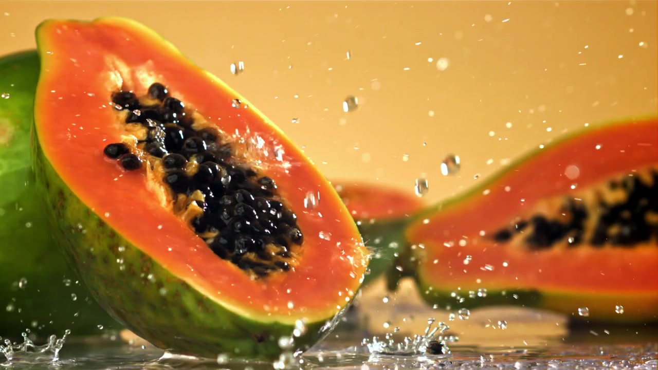 Ferske papaya-halvdeler med vannsprut i sakte film