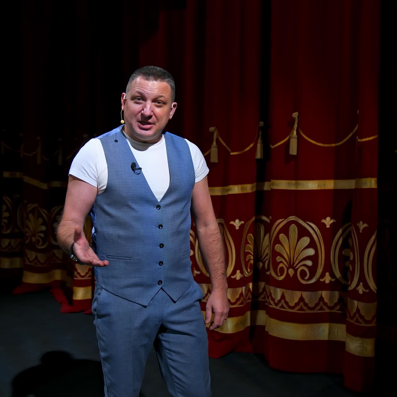 Man in front of empty theatre hall with red velvet chairs. Actor is standing on stage and talking with gestures before the performance