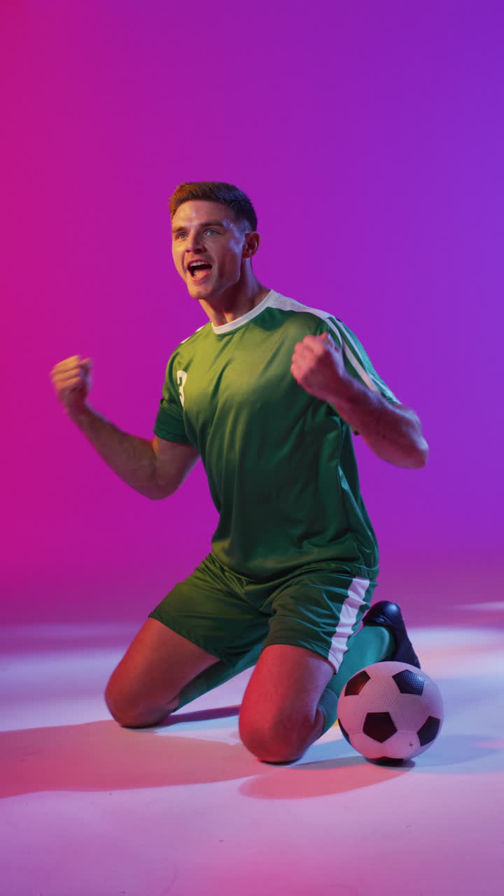 video verticale di un giocatore di calcio maschio caucasico felice con il calcio sopra l'illuminazione rosa al neon