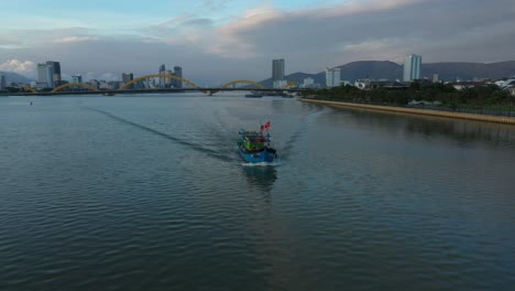 aerial orbit shot around a fishing boat at sunset with the city skyline of vietnam in background