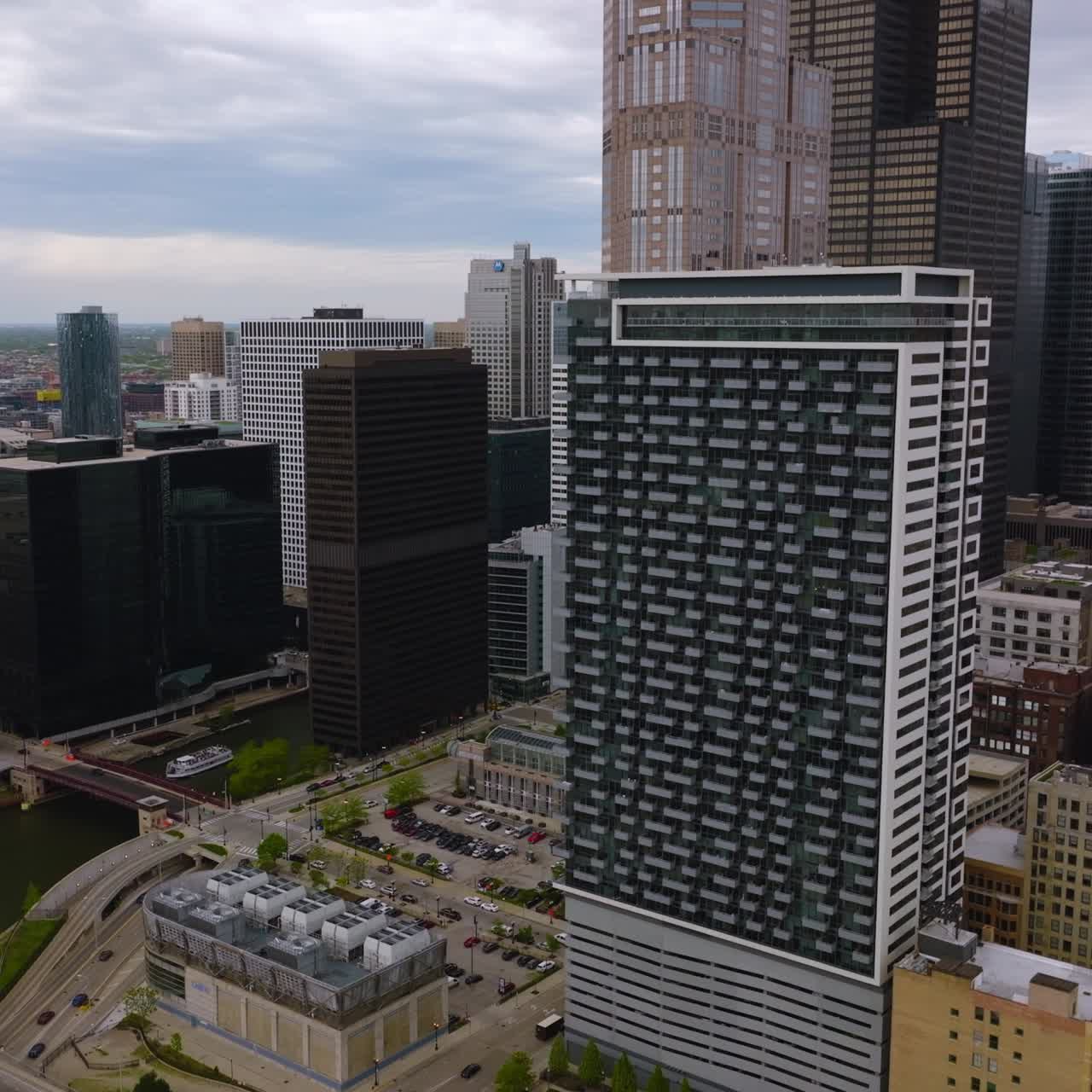 Narrow river flowing among the buildings of Chicago downtown. Multiple cars going by the bridge and highways and standing at parking lots