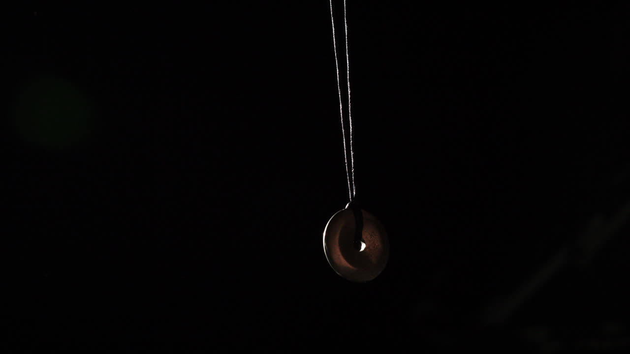 Pendulum used for hypnotism and readings swinging against black background