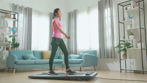 vista lateral de una mujer asiática entrenando en una cinta de correr en casa