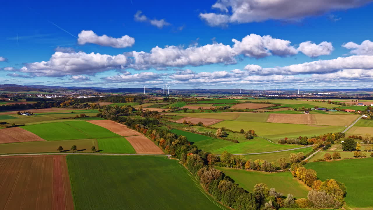 Vibrant countryside landscape with lush green fields and rolling hills under a bright blue sky filled with fluffy clouds