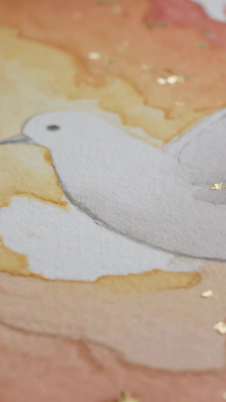 Vertical video: Panning camera revealing white dove watercolor on tabletop to show gold leaf detail