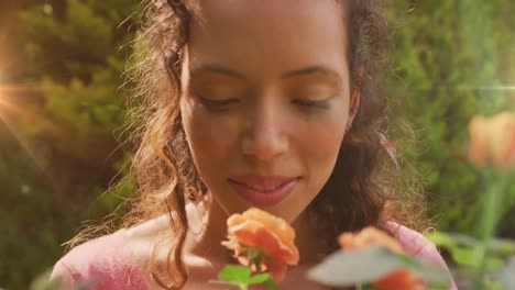 animation of light spots over biracial woman smelling flowers in garden