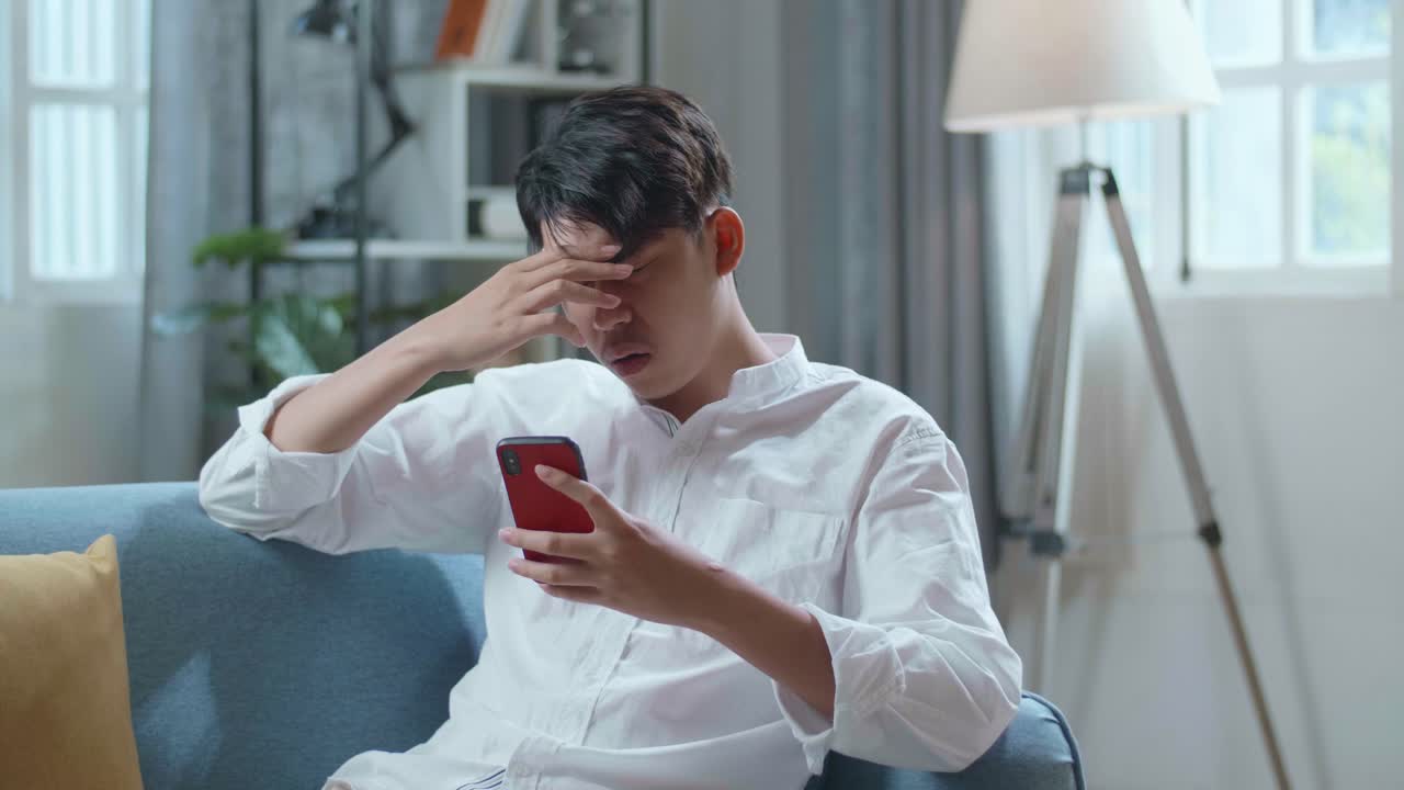 Asian Man Being Tired While While Lying On Sofa And Using Smartphone In The Living Room