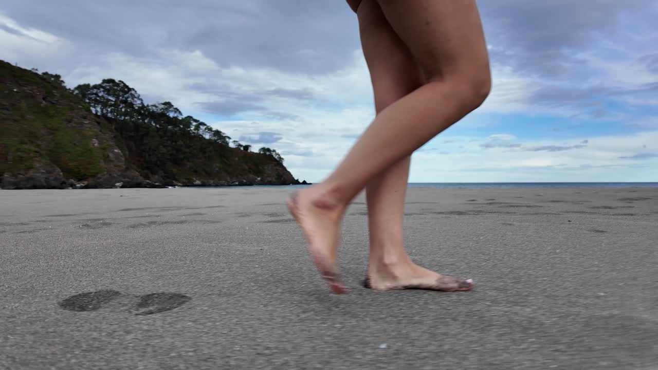 Slow-motion shot of a barefoot woman walking on an empty beach, symbolizing hope, direction, and moving forward