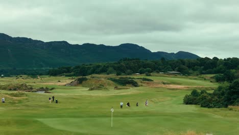 drone view of group of golfers and caddies walking towards green from fairway through rolling hills of ireland links golf course