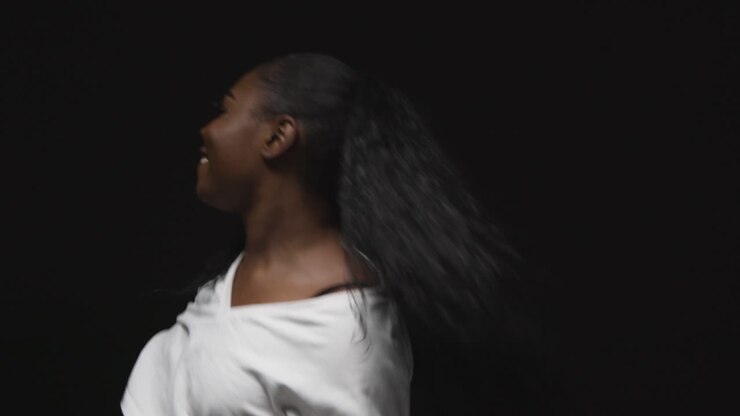 Primer plano de estudio de mujer joven bailando con iluminación de clave baja contra un fondo negro.