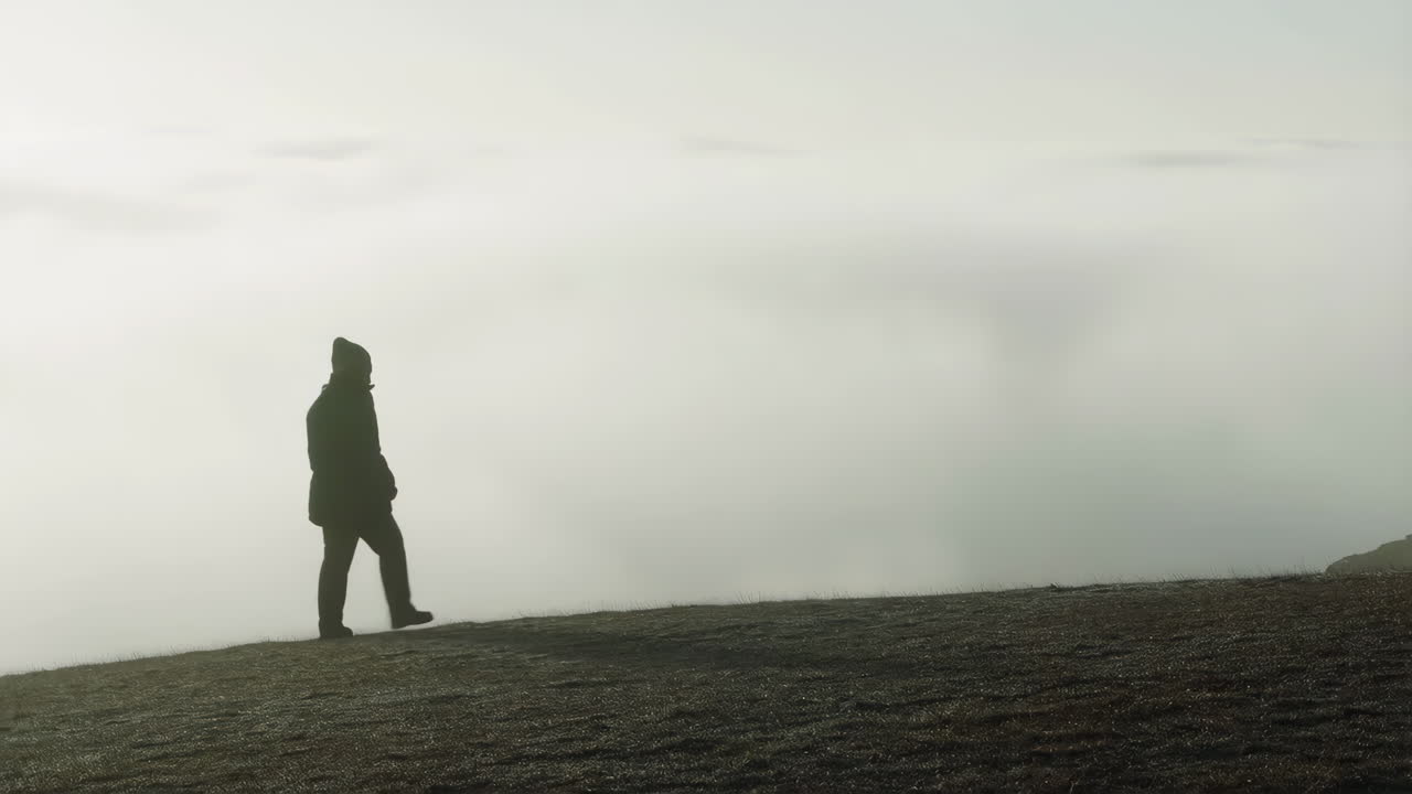 Silhouette of a person walking on a foggy hill
