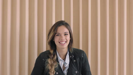 Lindo-Retrato-De-Mujer-Hispana-De-Una-Hermosa-Joven-Sonriendo-Alegre-A-La-Cámara-Con-Una-Elegante-Chaqueta-De-Cuero-En-Un-Fondo-De-Madera