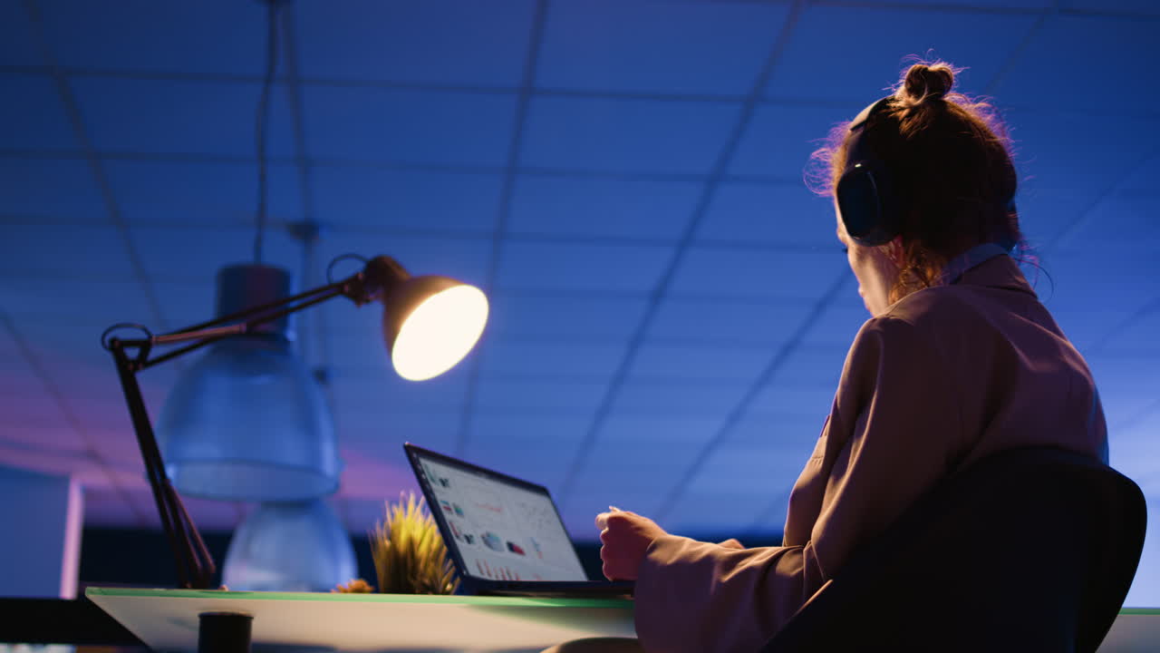 Woman working late at night in the office with laptop and headphones