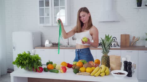 sporty woman standing near fruits. happy young woman with muscular body standing in the kitchen
