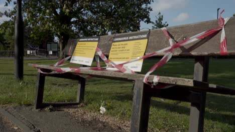 a caucasian woman jogging in a park past a bench which has been closed due to coronavirus lockdown in london