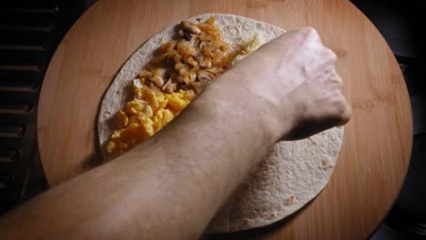 preparing delicious quesadilla recipe with scrambled eggs, mushroom, and cheese on tortilla wrap