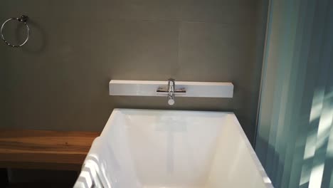 modern and elegant white bathtub is shown in a hotel bathroom, featuring a wooden bench, a towel rack, and a contemporary faucet, creating a relaxing and luxurious atmosphere