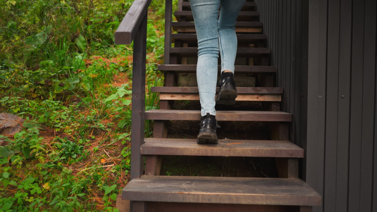 Woman climbs house stairs backside view. Lady comes home hopping after relaxing during walk in forest area. Scent of pine needles and earth lingers in air